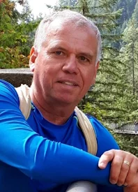 Man hiking in forest with blue shirt and backpack.