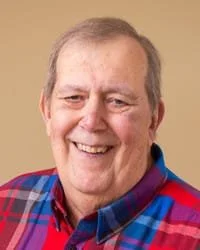 Smiling person in plaid shirt, beige background.