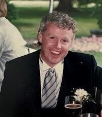 Smiling man in suit at outdoor event.