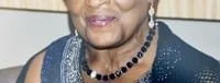 Elderly person wearing earrings and necklace, smiling.