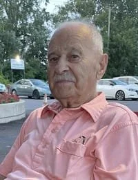 Elderly man sitting outside near parked cars.