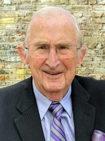 Elderly man in suit with brick wall background.