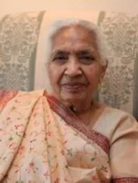 Elderly woman sitting, smiling in traditional attire.