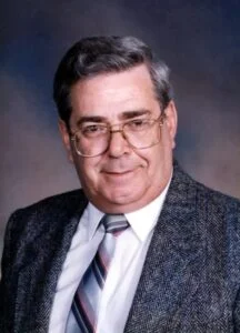 Elderly man in suit and glasses with gray hair.