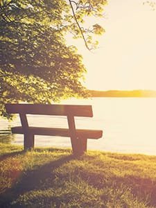 Wooden bench by a sunlit lake view.