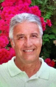 Smiling man in front of vibrant pink flowers.