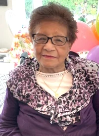 Elderly woman smiling indoors with colorful balloons.