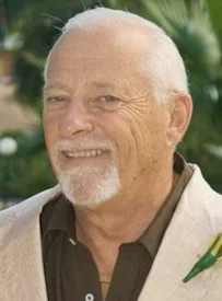 Smiling older man with white beard and tropical background.