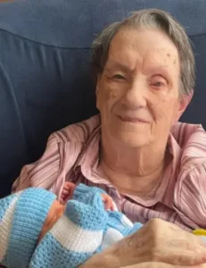 Elderly woman holding newborn baby wearing blue hat.