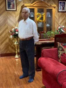 Elderly man in living room with number 21 balloons.