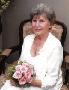 Elderly woman smiling and holding pink roses.