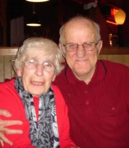 Smiling elderly couple in red shirts hugging.