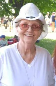 Smiling woman in sunglasses and white hat outdoors.