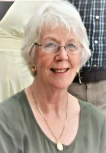 Smiling woman with glasses and short white hair.