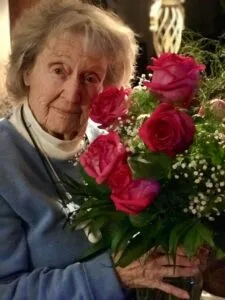 Elderly woman holding pink roses bouquet.