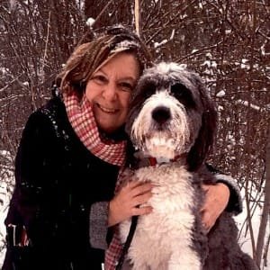 Person hugging large fluffy dog in snowy woods.