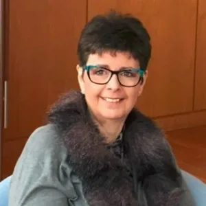 Smiling person wearing glasses and fur collar.