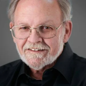 Elderly man with glasses and beard smiling.