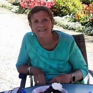 Smiling person seated outdoors with colorful flowers.