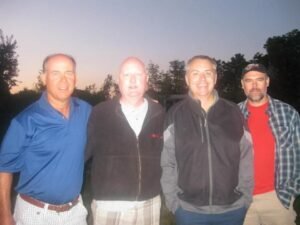 Four men posing outdoors at dusk.