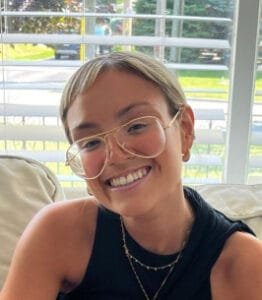 Person smiling with glasses and short hair indoors.