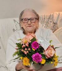 Elderly woman holding colorful floral arrangement, smiling gently.