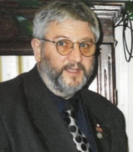 Man in suit with glasses standing indoors.