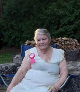 Elderly woman with birthday ribbon sitting outdoors.