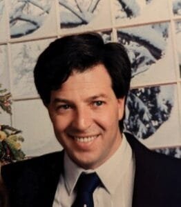 Smiling man in suit, snowy window background.