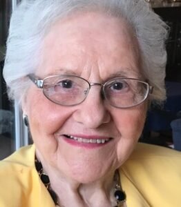 Elderly woman smiling with glasses and yellow jacket