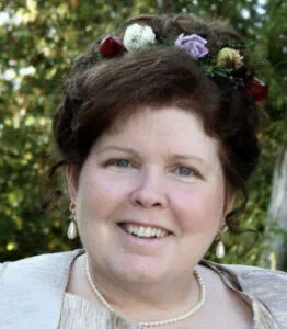 Woman smiling outdoors with floral hair decoration.