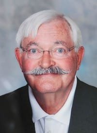 Elderly man with glasses and a mustache smiling.