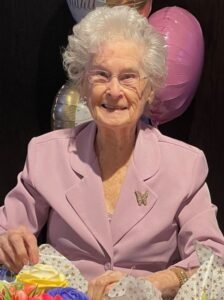 Elderly woman in pink suit with balloons.