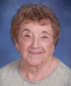 Elderly woman with curly hair smiling.