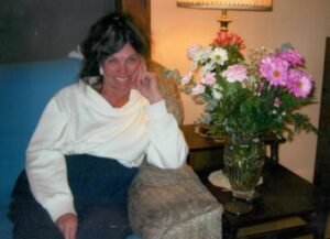 Person relaxing on a chair beside flowers indoors.