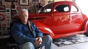 Man sitting in garage with vintage red car.