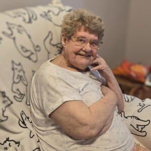 Elderly woman smiling on a patterned blanket.