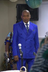 Man in blue suit at event with microphone.