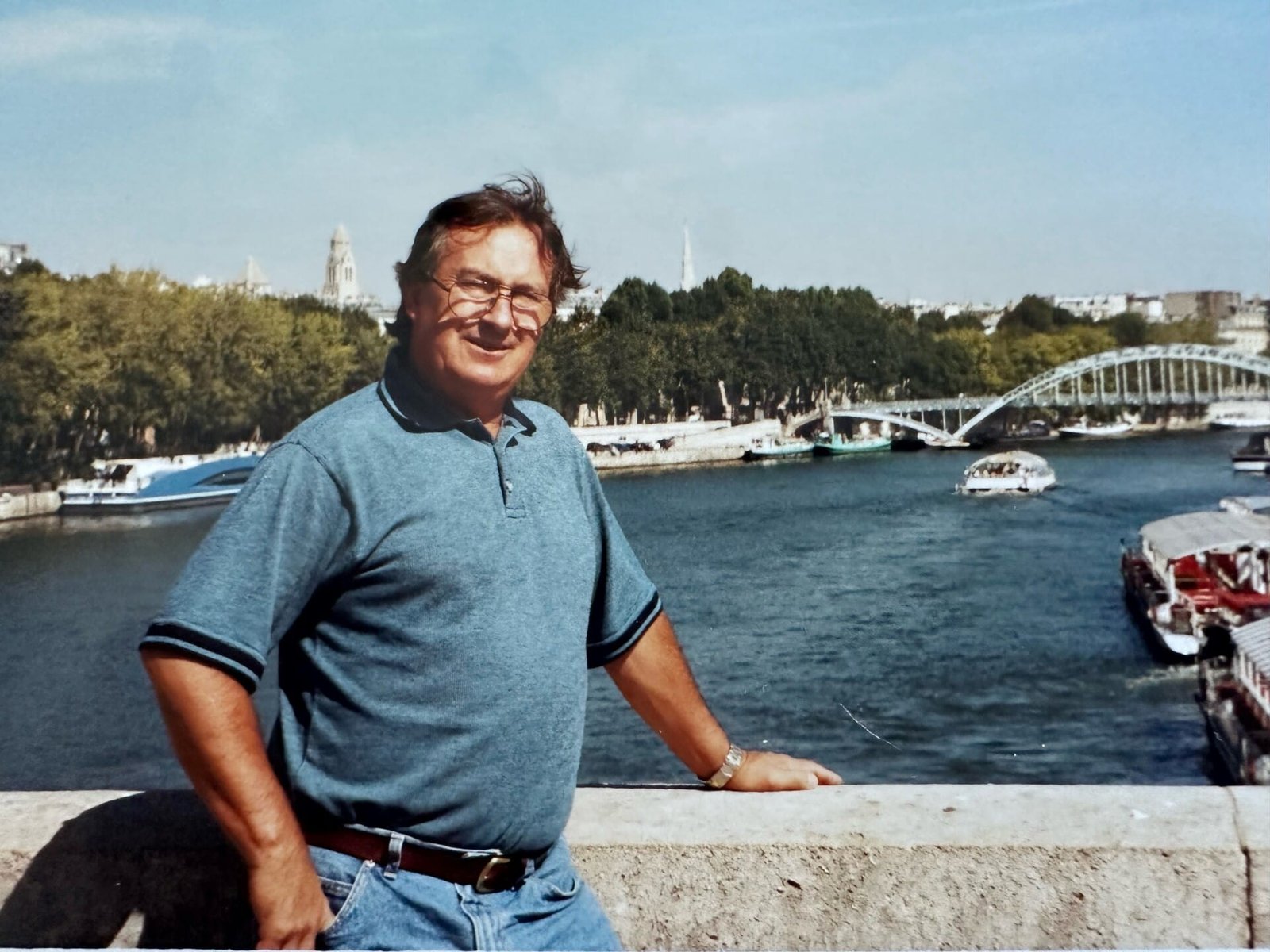 Smiling man by a riverside bridge.