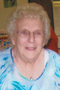 Elderly woman smiling indoors, wearing glasses.