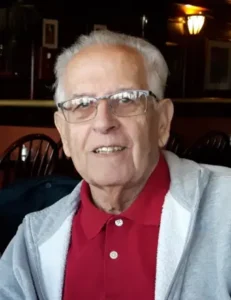 Elderly man wearing glasses and red shirt indoors.