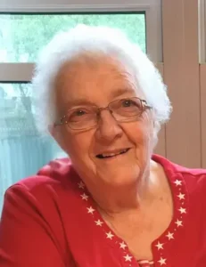 Smiling elderly woman with glasses and white hair.