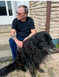 Man sitting with large black dog outdoors.