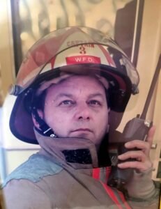 Firefighter holding radio, wearing helmet and uniform.